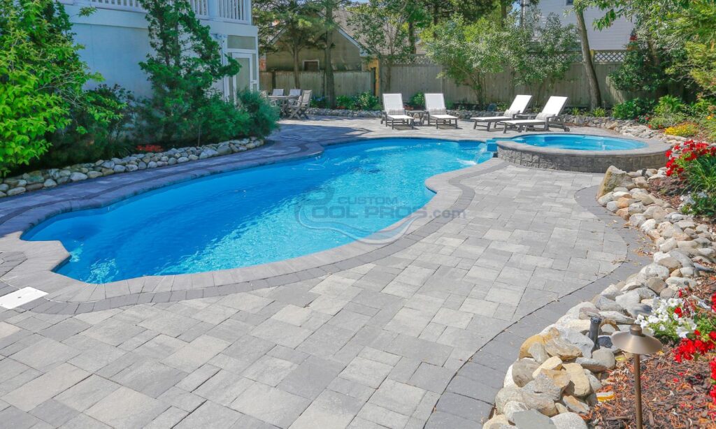 Luxury backyard pool with a curved shape, surrounded by stone pavers and lounge chairs, set in a landscaped garden. Perfect for relaxation and outdoor entertaining, swimming pool construction nj
