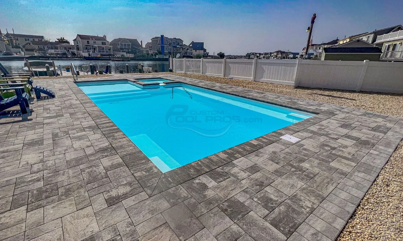 Bright blue swimming pool surrounded by modern stone patio, with clear skies and buildings visible in the background, ideal for outdoor relaxation and leisure activities, pool installers
